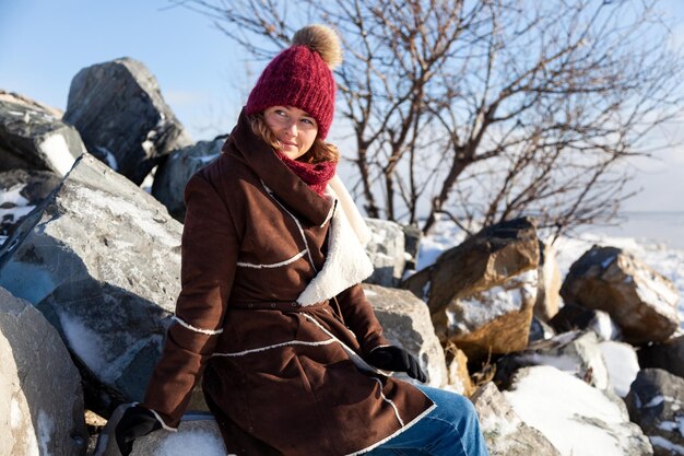 Portrait en gros plan extérieur d'une belle jeune femme aux cheveux longs portant un manteau de chapeau posant le concept de marche d'hiver de Noël en pierre d'hiver