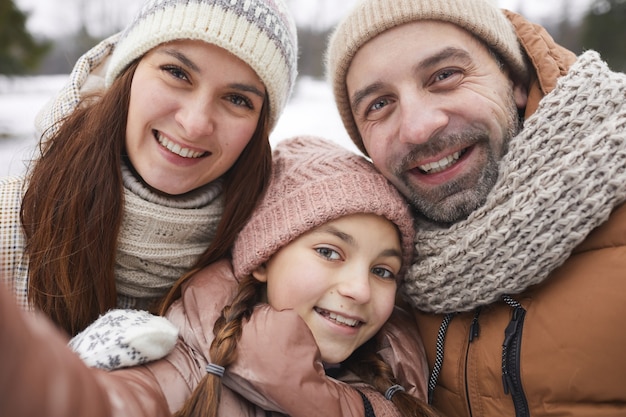 Portrait en gros plan d'une famille heureuse prenant une photo de selfie et souriant à la caméra tout en profitant d'une promenade en plein air ensemble dans la forêt d'hiver