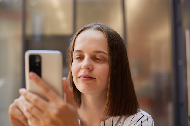 Portrait en gros plan d'une femme d'affaires aux cheveux bruns utilisant un téléphone portable regardant l'écran d'un smartphone avec une expression positive concentrée