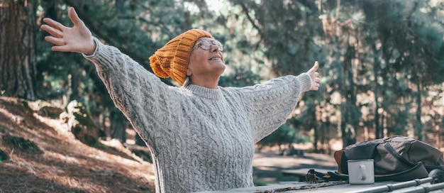 Portrait en gros plan d'une femme d'âge moyen qui s'amuse et se détend assise à table dans la nature dans la forêt de montagne Vieille personne féminine ouvrant les bras se sentant libre Concept de vie de liberté