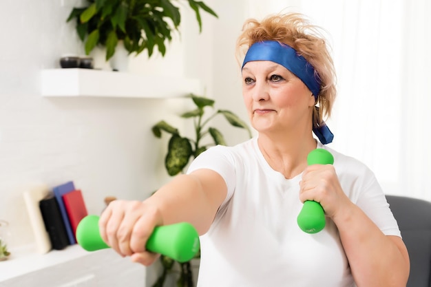 Portrait en gros plan d'une femme âgée active faisant des exercices d'haltères à la maison, souriante.