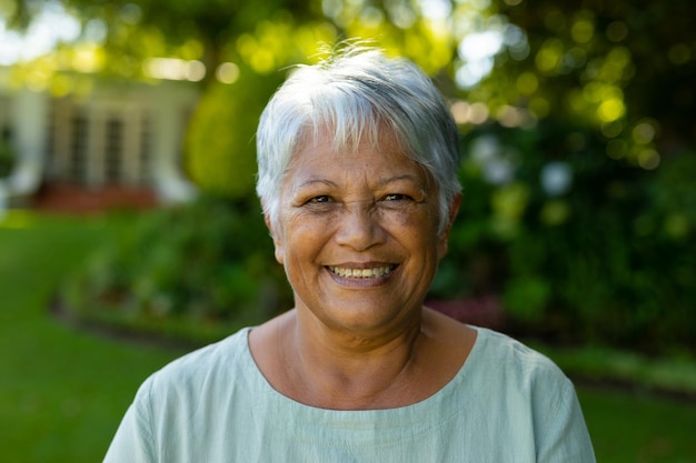 Portrait en gros plan d'une femme âgée biraciale souriante aux cheveux gris courts contre des arbres dans le parc