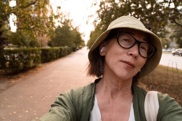 Portrait en gros plan d'une femme asiatique senior souriante en chapeau et lunettes parlant pendant un appel vidéo