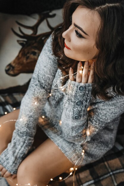 Portrait en gros plan d'une femme assise confortablement avec des guirlandes lumineuses.