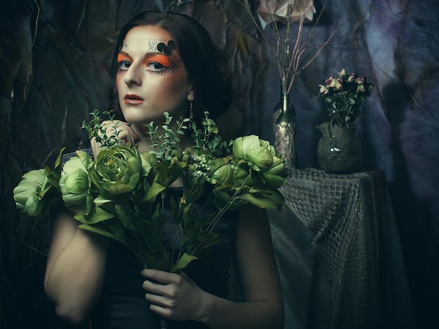 Portrait en gros plan d'une femme aux cheveux roux avec un maquillage créatif lumineux tenant des fleurs sèches