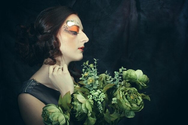 Portrait en gros plan d'une femme aux cheveux roux avec un maquillage créatif lumineux tenant des fleurs sèches