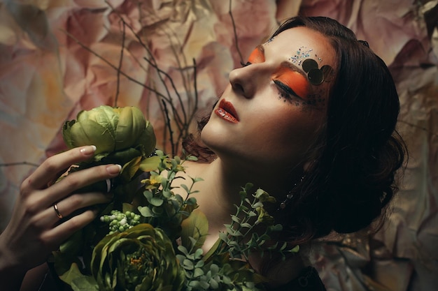 Portrait en gros plan d'une femme aux cheveux roux avec un maquillage créatif lumineux tenant des fleurs sèches