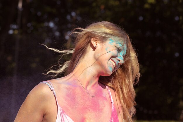 Portrait en gros plan d'une femme blonde positive avec du vent dans les cheveux posant sur le festival Holi