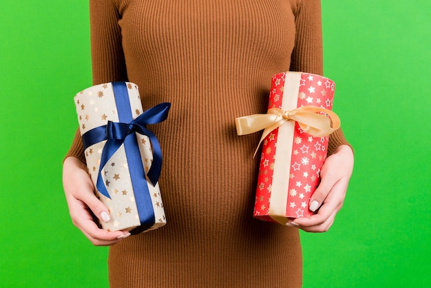 Portrait en gros plan d'une femme enceinte en robe marron tenant deux coffrets cadeaux sur fond vert En attente d'un petit garçon ou d'une petite fille Attendant des jumeaux Copier l'espace