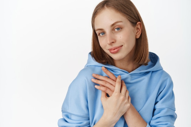 Portrait en gros plan d'une femme mignonne tendre et féminine, se tenant la main près de la poitrine, souriante sensuelle et rêveuse, regardant heureuse devant