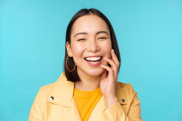 Portrait en gros plan d'une fille asiatique naturelle qui rit en souriant et qui a l'air heureuse debout sur fond bleu Copiez l'espace