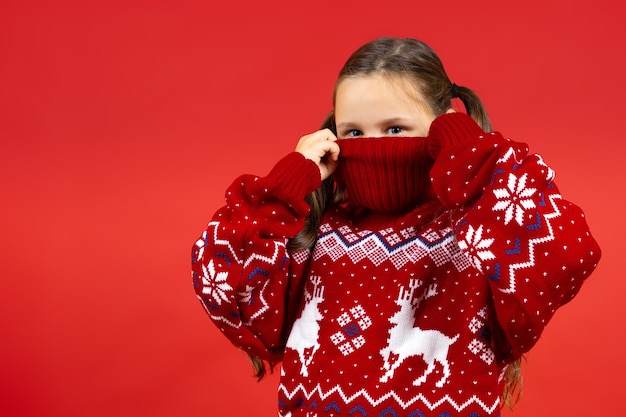 Photo portrait en gros plan d'une fille enjouée cachant la moitié du visage en pull de noël rouge avec renne isolé...