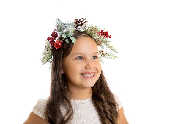 Portrait en gros plan d'une fille souriante de profil d'enfant en guirlande de Noël et robe blanche en détournant les yeux avec...