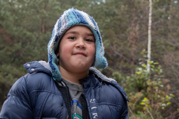 Photo portrait en gros plan d'un garçon portant un chapeau de tricot alors qu'il se tient contre des arbres