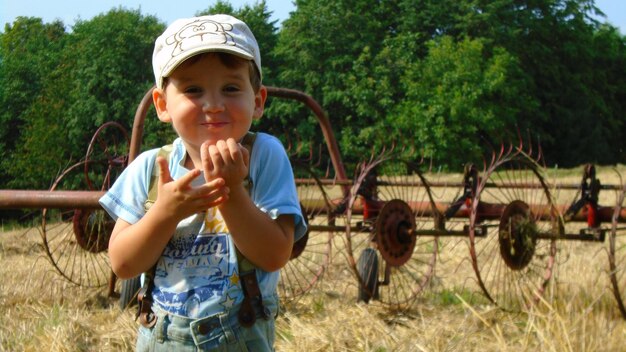 Photo portrait en gros plan d'un garçon souriant alors qu'il se tient contre des machines agricoles sur le champ