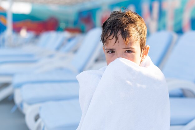 Portrait en gros plan d'un garçon souriant enveloppé dans une serviette après avoir nagé dans la piscine extérieure