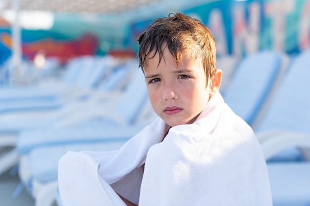 Portrait en gros plan d'un garçon souriant enveloppé dans une serviette après avoir nagé dans la piscine extérieure