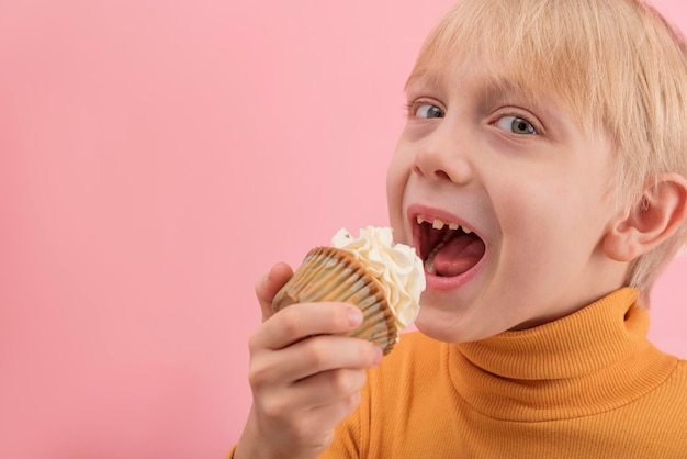 Portrait gros plan garçon veut manger cupcake Enfant blond avec muffin dans ses mains sur fond rose Copy space