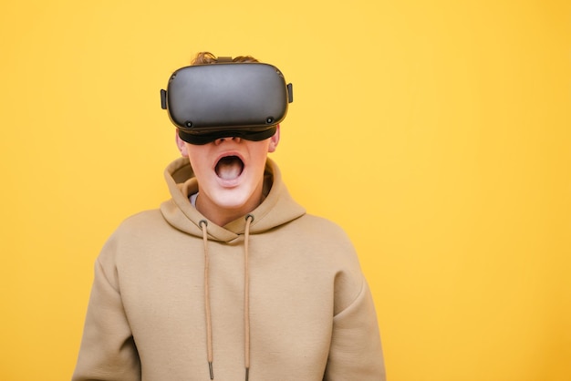 Portrait en gros plan d'un gars choqué dans un casque VR sur fond jaune regardant dans l'espace de copie de la caméra à côté Joueur adolescent émotionnel jouant à des jeux dans un casque VR