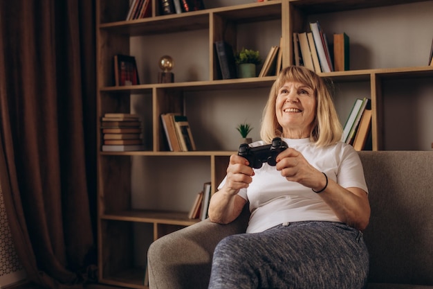 Portrait en gros plan d'une grand-mère aînée excitée avec un sourire à pleines dents jouant au jeu vidéo au studio isolé sur fond beige Concept de joueur de console de joueur