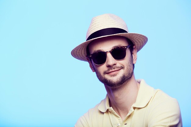 Portrait en gros plan d'un hipster génial portant un chapeau fedora avec un regard intense sur la tête de l'appareil photo sur fond de studio bleu