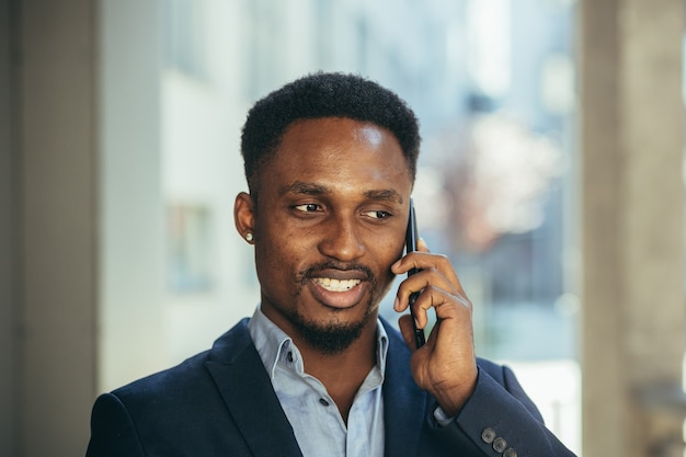 Portrait en gros plan d'un homme d'affaires africain parlant au téléphone et souriant du succès en costume d'affaires