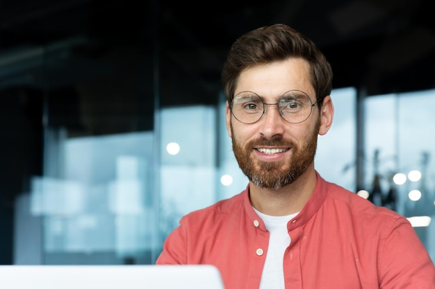 Portrait en gros plan d'un homme d'affaires mature à l'intérieur d'un homme de bureau avec barbe et chemise rouge souriant et