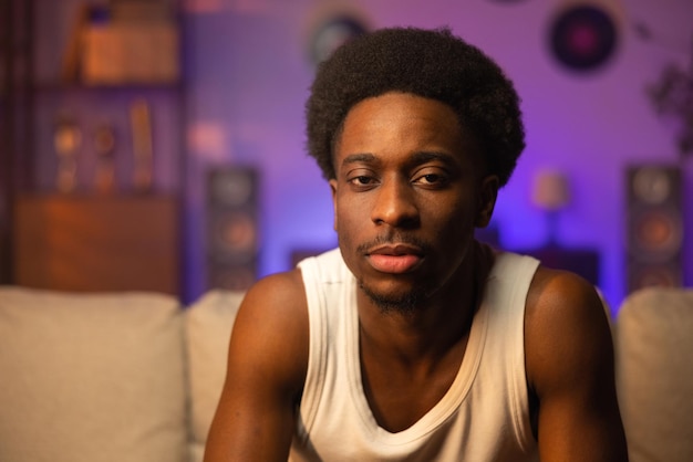 Portrait en gros plan d'un homme afro assis sur un canapé portant une chemise sans bretelles blanche