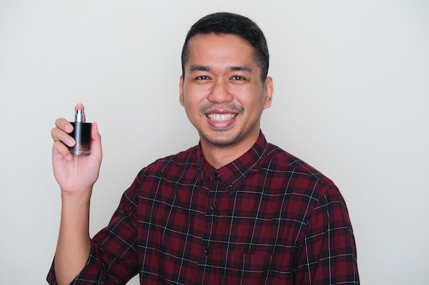 Photo portrait en gros plan d'un homme asiatique adulte souriant confiant tout en montrant sa bouteille de parfum