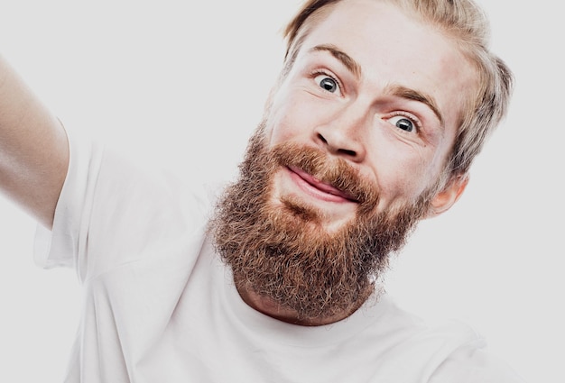 Portrait en gros plan d'un homme barbu joyeux prenant selfie sur fond blanc