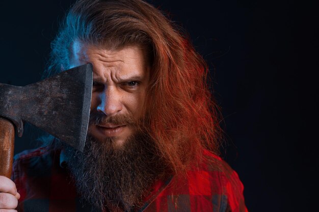 Portrait en gros plan d'un homme brutal émotionnel aux cheveux longs qui tient une vieille hache bûcheron barbu