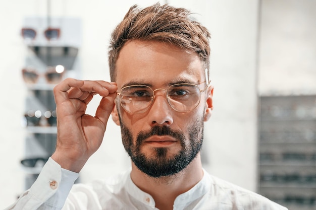 Portrait en gros plan d'un homme élégant avec barbe choisissant des lunettes dans le magasin d'optique