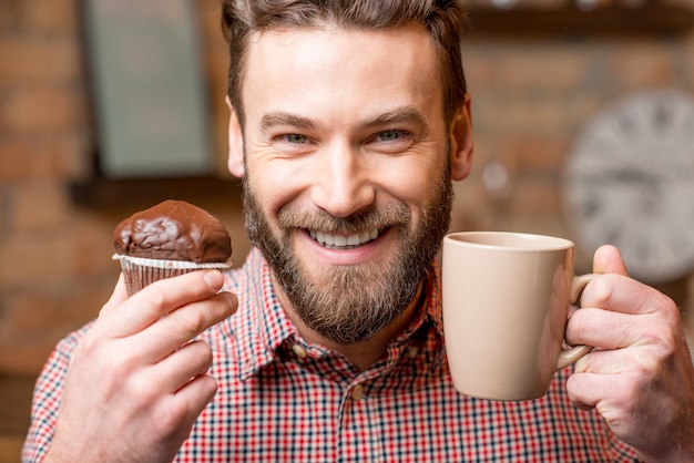 Portrait en gros plan d'un homme avec un muffin au chocolat et une tasse de café à la cuisine