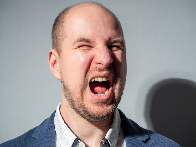 Portrait en gros plan d'un homme de race blanche dans une veste qui crie furieusement. Agression, défi, émotion.