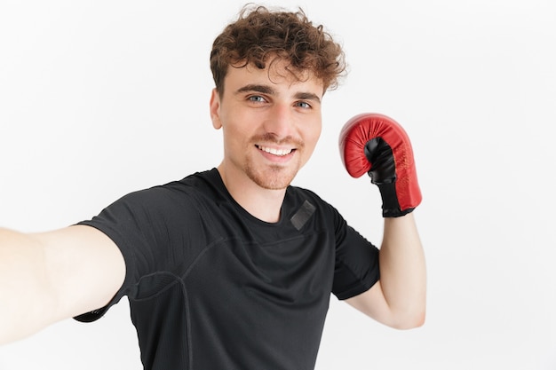 Portrait en gros plan d'un homme sportif brune en t-shirt souriant et prenant selfie Portrait en gant de boxe isolé sur mur blanc