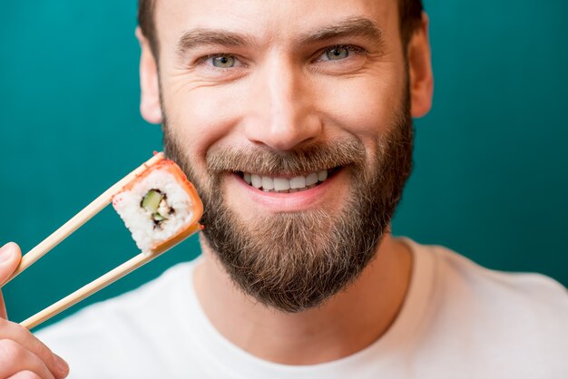 Portrait en gros plan d'un homme tenant des sushis avec des baguettes sur le fond vert