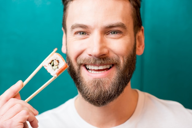 Portrait en gros plan d'un homme tenant des sushis avec des baguettes sur le fond vert