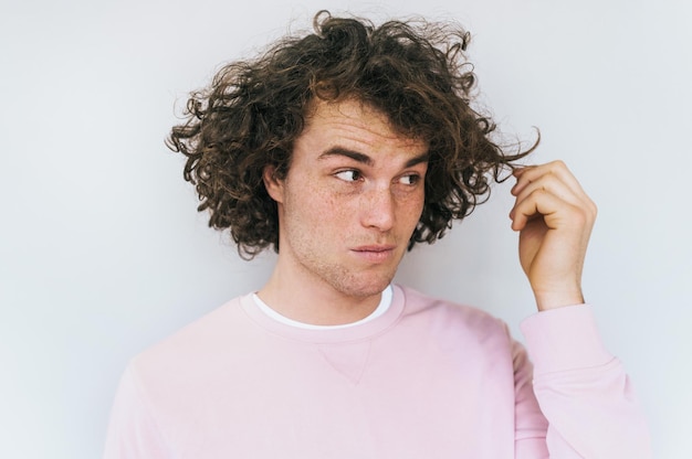 Portrait en gros plan horizontal d'un homme mécontent élégant aux cheveux bouclés pose en studio sur fond blanc montre que ses cheveux endommagés ont besoin d'un traitement Désaccord et expressions négatives