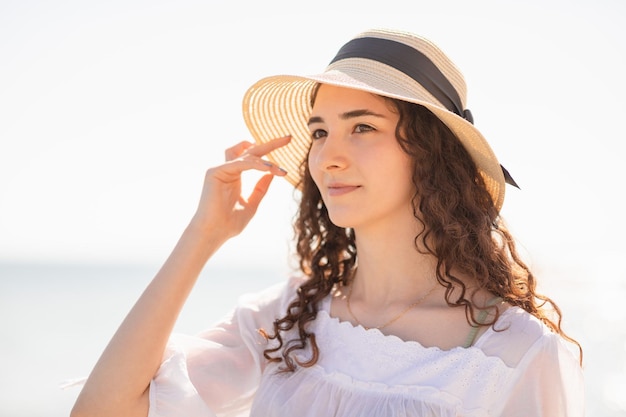 Photo portrait en gros plan d'une jeune adolescente brune aux cheveux bouclés et chapeau de paille à la journée ensoleillée