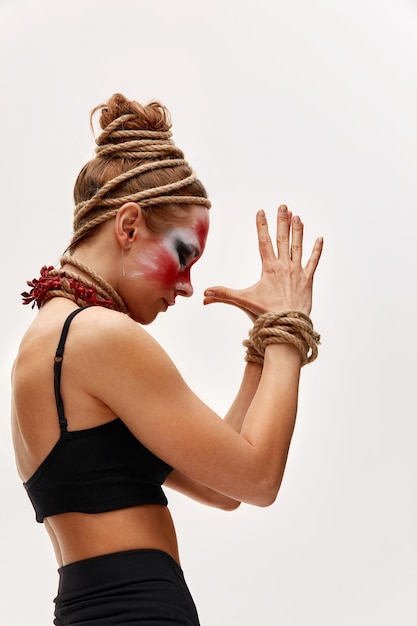 Portrait en gros plan d'une jeune belle fille avec une peinture de visage colorée Halloween maquillage professionnel les cheveux dans le cou de peinture et les mains sont enveloppées avec des cordes Concept de victime