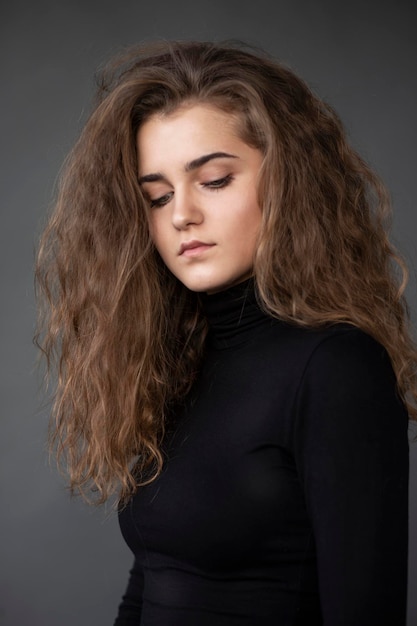 Portrait en gros plan d'une jeune femme aux cheveux bouclés portant une valise noire isolée sur fond gris regardant vers le bas