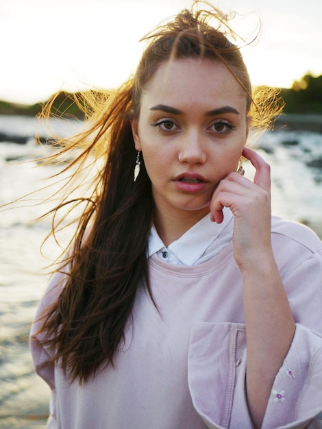 Portrait en gros plan d'une jeune femme aux cheveux en désordre debout contre la mer