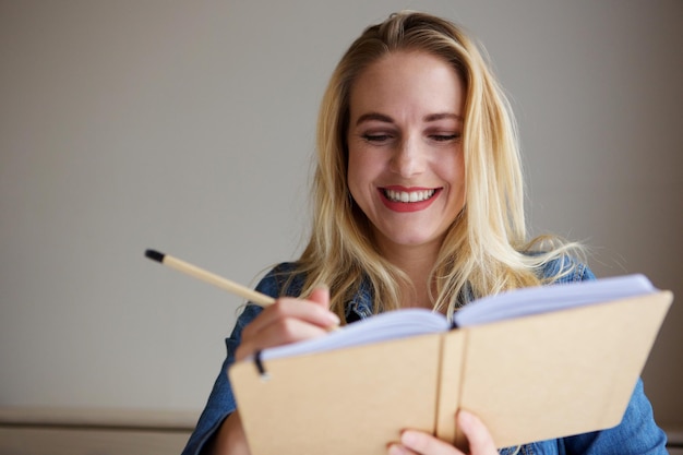 Portrait en gros plan d'une jeune femme blonde heureuse écrivant dans un livre