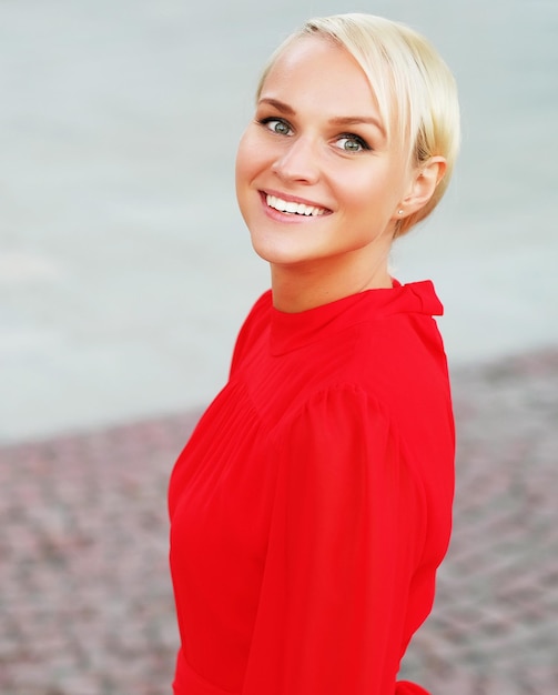 Portrait en gros plan d'une jeune femme blonde heureuse portant une robe rouge avec un sourire joyeux