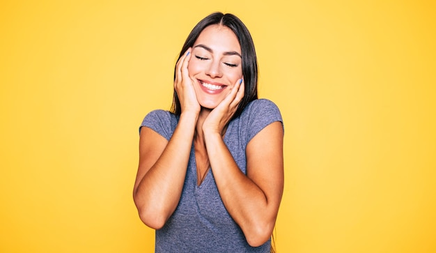 Portrait en gros plan d'une jeune femme brune mignonne séduisante et souriante en T-shirt gris pose et regarde la caméra isolée sur un mur jaune