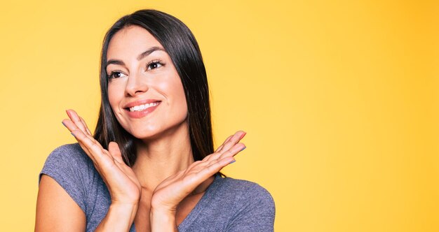 Portrait en gros plan d'une jeune femme brune mignonne séduisante et souriante en T-shirt gris pose et regarde la caméra isolée sur un mur jaune