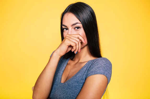 Portrait en gros plan d'une jeune femme brune mignonne séduisante et souriante en T-shirt gris pose et regarde la caméra isolée sur un mur jaune