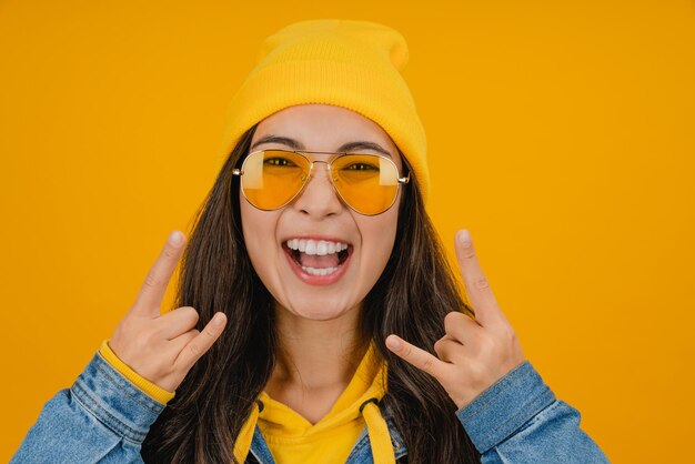 Portrait en gros plan d'une jeune femme sur fond jaune isolé faisant un geste de rock