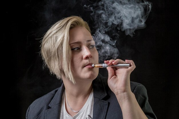 Photo portrait en gros plan d'une jeune femme fumant sur un fond noir