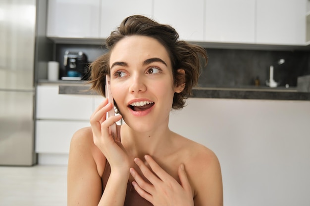 Portrait en gros plan d'une jeune femme parlant sur un téléphone mobile qui a l'air surpris d'entendre des nouvelles étonnantes assis